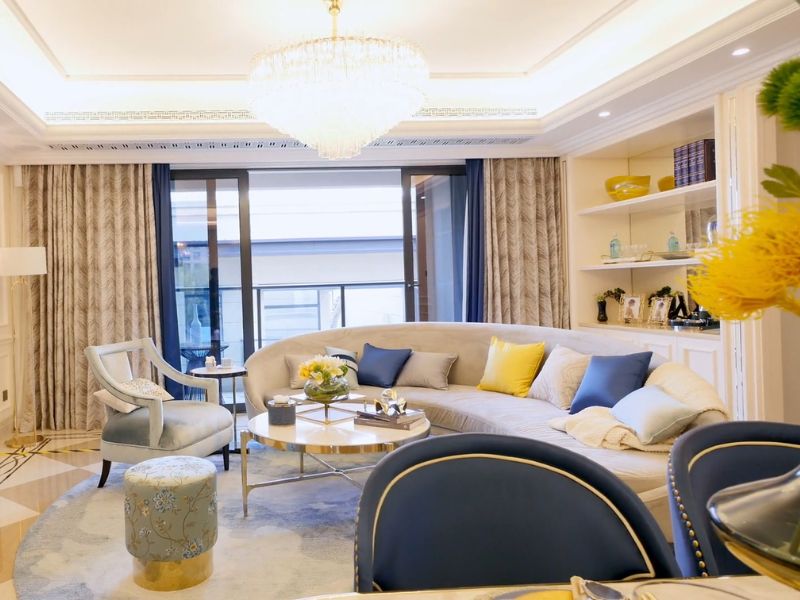 prikaz moderno sređene dnevne sobe sa velikom belom ugaonom i jastucima na njoj, pored je tabure i sto za ručavanje